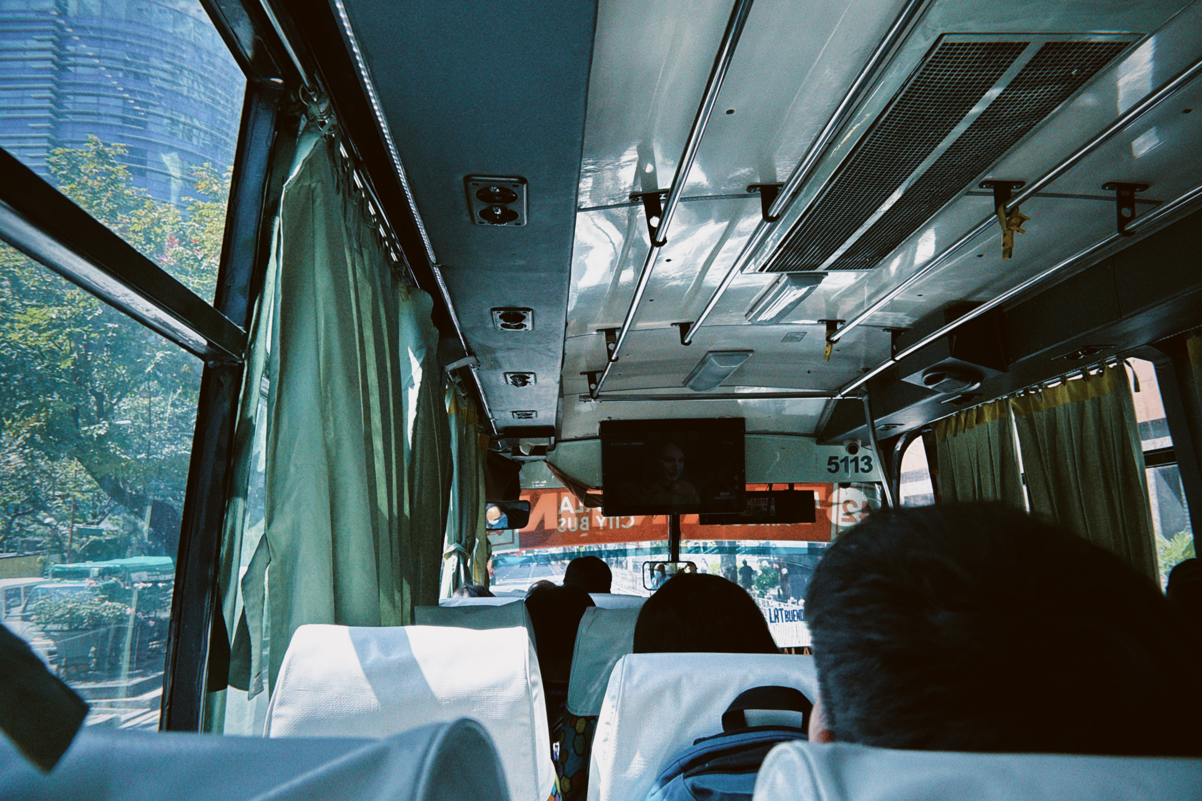 View from inside a Manila city bus, looking toward the front with passengers seated and the city visible through the window