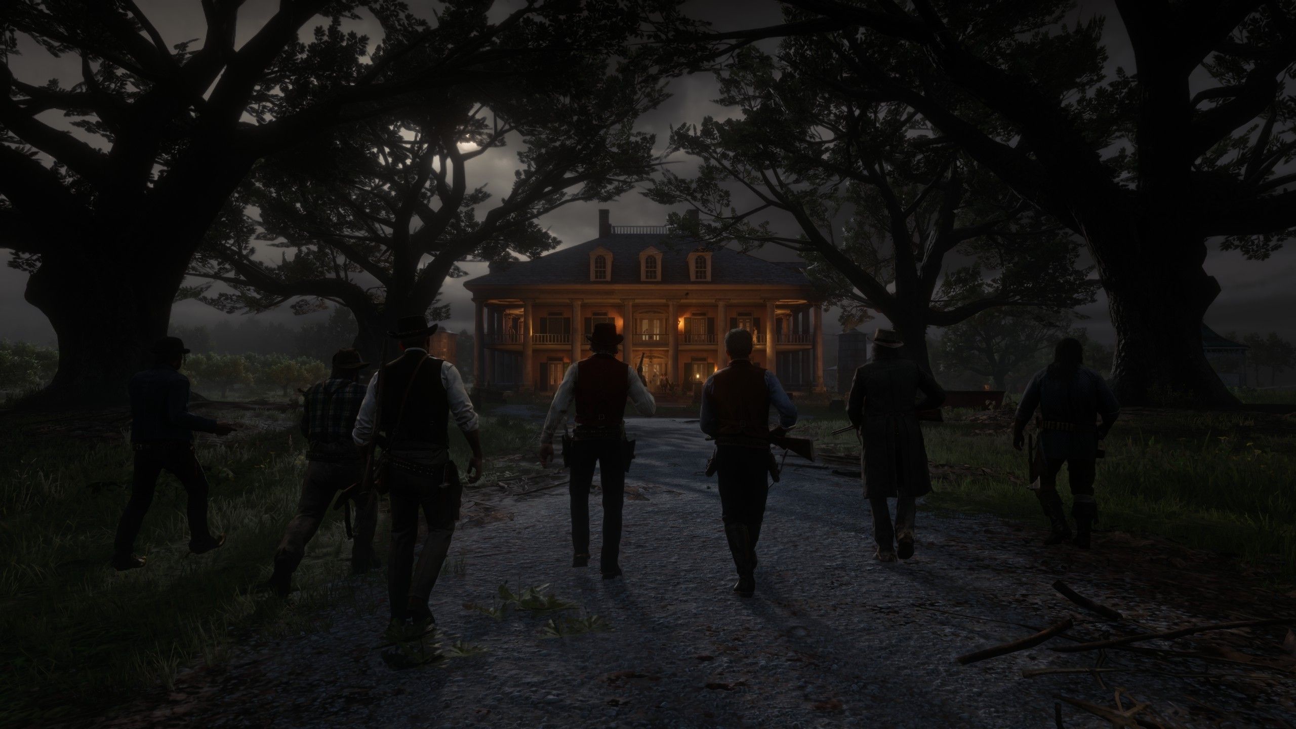 The gang approaching Braithwaite Manor beneath large trees at night in Red Dead Redemption 2